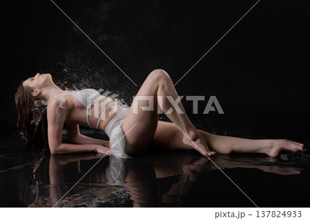 Sensual woman in white lingerie lying on a reflective surface with a dramatic water splash. Sensual woman in white lingerie lying on a reflective surface with a dramatic water splash. 137824933