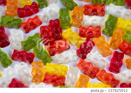 Multicolored gummy bears resting on whipped cream texture, contrast between translucent candies and fluffy white surface, mouthwatering dessert concept with vibrant tones 137825012