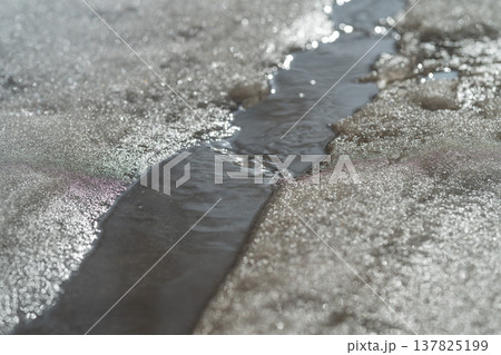 Path of flowing meltwater through snow with textures and lines. Meandering meltwater stream carving through snow with visible current patterns and contrasting textures 137825199