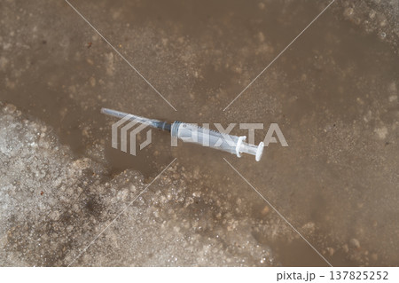 Discarded syringe reflects environmental neglect and pollution concerns. An abandoned syringe in muddy puddle highlights urban environmental degradation and health hazards 137825252
