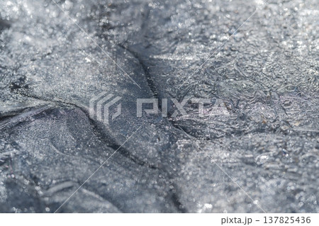 Ice flows shimmer. Melting ice forms ridges and shimmering wet lines in sunlight. Soft light reveals tactile flow patterns and radiant melt currents in swirling spring ice 137825436