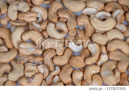 Golden brown nut pattern. Detailed photograph showcasing crispy roasted nut textures. Closeup macro shot capturing warm tones and textured surfaces of roasted cashews Golden brown nut pattern. Detailed photograph showcasing crispy roasted nut textures. Closeup macro shot capturing warm tones and textured surfaces of roasted cashews 137825505