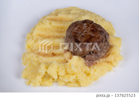 Small meat serving. Compact portion of browned meat placed over textured mashed potatoes. Miniature meat patty served atop creamy ridged mashed potatoes as small dish 137825523
