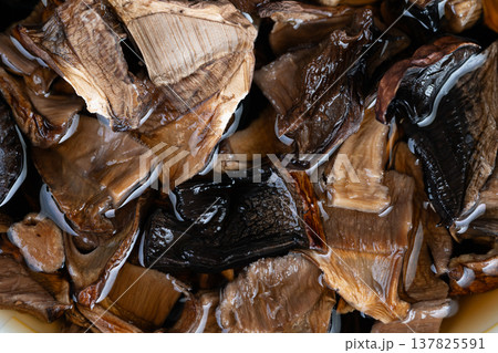 Dried fungi submerged creating savory infusion for culinary use. Rehydrating dried mushrooms releases concentrated savory notes for soups and sauces preparation 137825591