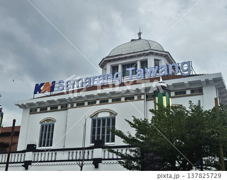The historic Semarang Tawang Railway Station in Indonesia features magnificent Dutch colonial architecture with its iconic large dome and vintage windows under a dramatic cloudy afternoon sky. 137825729
