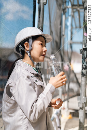 建設現場での徹底した体調管理。水分補給と適度な休息で熱中症を予防する女性職人 137827523