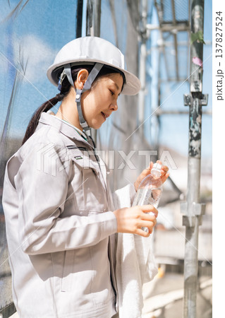 建設現場での徹底した体調管理。水分補給と適度な休息で熱中症を予防する女性職人 137827524