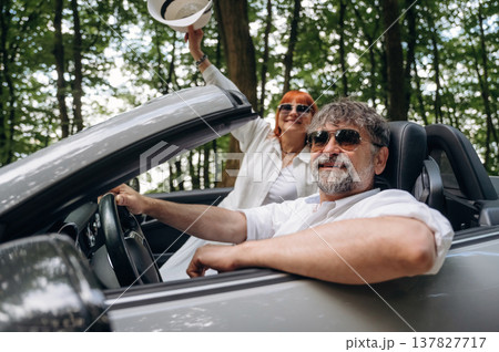 Hands are up, happy woman is with hat. Senior couple driving convertible cabriolet car Hands are up, happy woman is with hat. Senior couple driving convertible cabriolet car 137827717