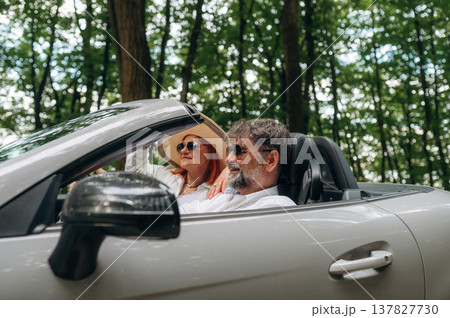 Road near the trees. Senior couple driving convertible cabriolet car 137827730