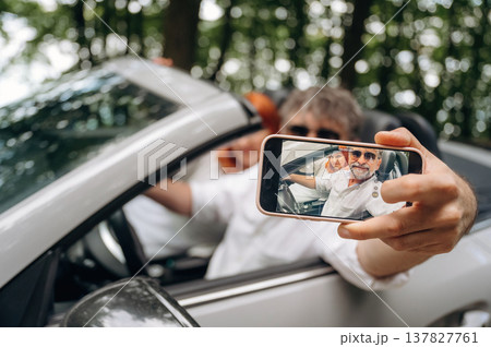 Smiling, doing selfie. Senior couple driving convertible cabriolet car Smiling, doing selfie. Senior couple driving convertible cabriolet car 137827761