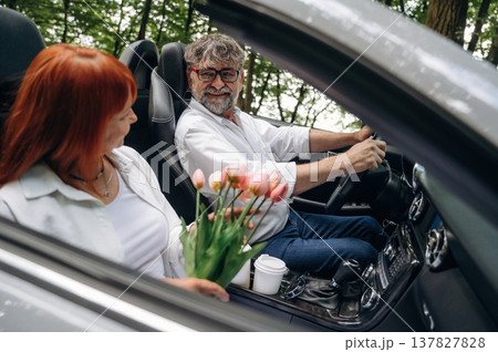 Flowers in hands. Senior couple driving convertible cabriolet car 137827828