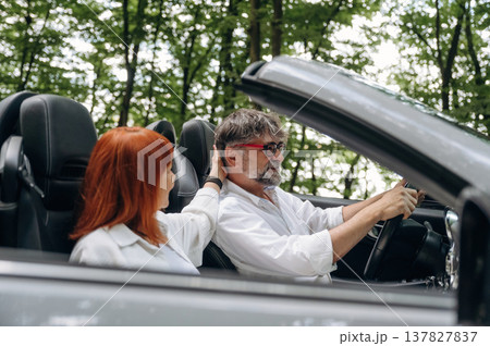 Touching the hair, conception of love and care. Senior couple driving convertible cabriolet car Touching the hair, conception of love and care. Senior couple driving convertible cabriolet car 137827837