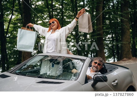 Shopping bags are in hands. Senior couple driving convertible cabriolet car Shopping bags are in hands. Senior couple driving convertible cabriolet car 137827860