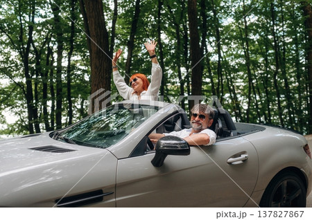 Road near the trees. Senior couple driving convertible cabriolet car 137827867