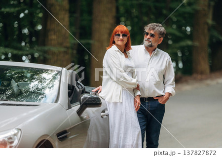 Lovely senior couple standing on the road near convertible cabriolet car Lovely senior couple standing on the road near convertible cabriolet car 137827872