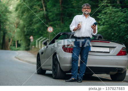 Man is standing near his cabriolet car on the road Man is standing near his cabriolet car on the road 137827883