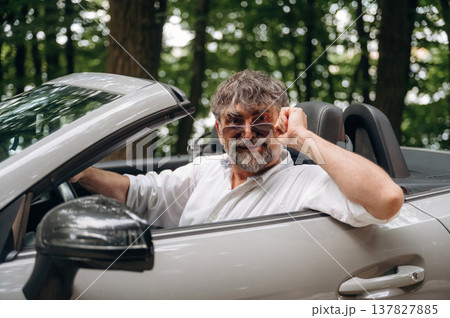 Beautiful, in sunglasses, looking at the camera. Stylish senior man is in convertible cabriolet car 137827885