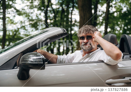 Beautiful, in sunglasses, looking at the camera. Stylish senior man is in convertible cabriolet car 137827886