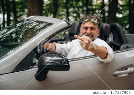 Middle finger up, don't care, cool attitude. Stylish senior man is in convertible cabriolet car Middle finger up, don't care, cool attitude. Stylish senior man is in convertible cabriolet car 137827909