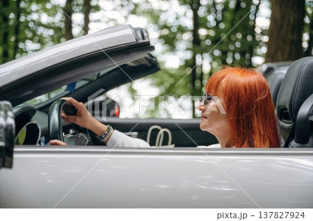 Having great time, in sunglasses. Side view of woman that is driving convertible cabriolet car 137827924