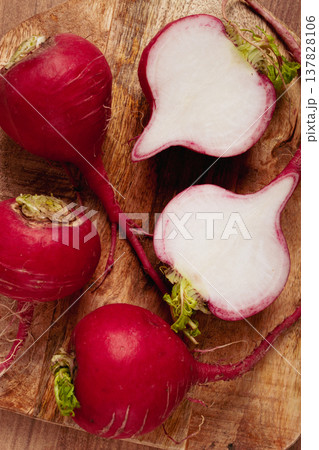 Freshly harvested red radishes on a wooden cutting board with one cut in half to reveal the white interior 137828106