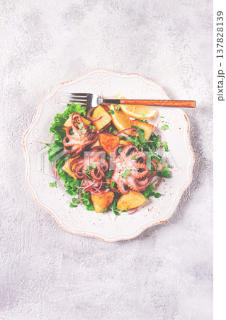 Grilled octopus with baked potatoes and fresh herbs, on a decorative light plate, homemade, no people 137828139