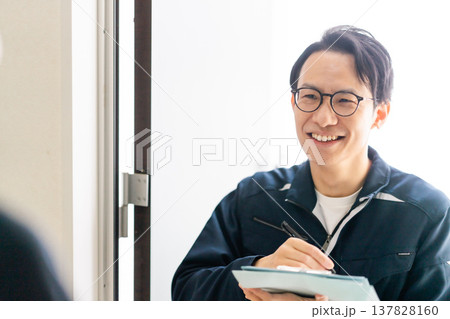 ライフラインの点検・訪問営業。クリップボードを手に、住宅の玄関先でヒアリングを行うエンジニア 137828160