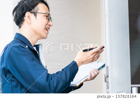 ライフラインの点検・訪問営業。クリップボードを手に、住宅の玄関先でヒアリングを行うエンジニア 137828164