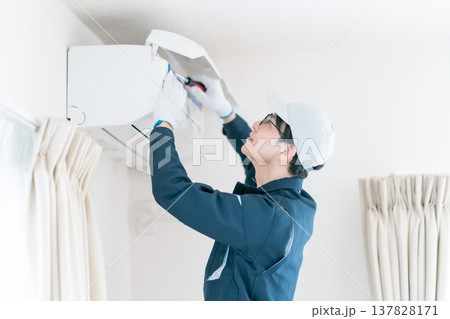 エアコンの内部点検。ドライバーを使って修理作業を行う作業服の男性エンジニア 137828171
