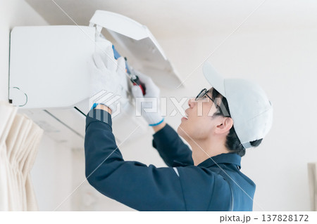 エアコンの内部点検。ドライバーを使って修理作業を行う作業服の男性エンジニア 137828172