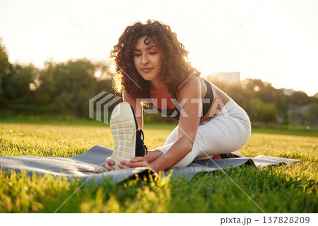 Stretching the legs. Young fitness woman is on the field outdoors Stretching the legs. Young fitness woman is on the field outdoors 137828209