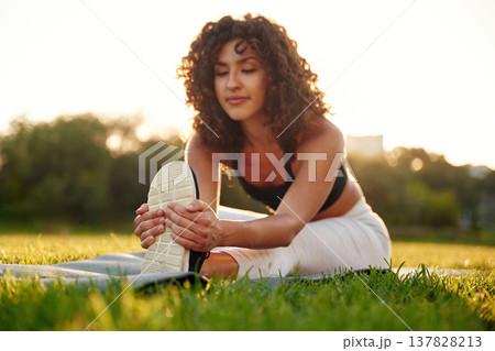 Flexibility exercise for legs. Young fitness woman is on the field outdoors 137828213