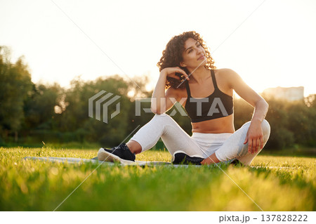 Sitting on the yoga mat. Young fitness woman is on the field outdoors 137828222