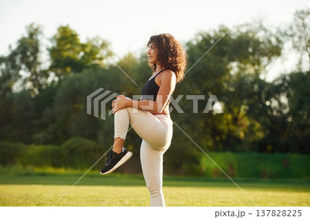 View from the side, doing fitness exercises. Young fitness woman is on the field outdoors 137828225