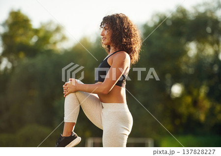 View from the side, doing fitness exercises. Young fitness woman is on the field outdoors 137828227