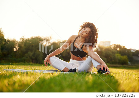 Sitting on the yoga mat. Young fitness woman is on the field outdoors 137828228