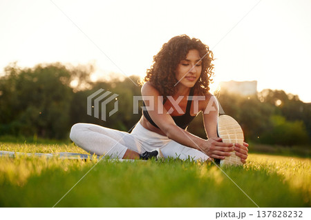 Sitting on the yoga mat. Young fitness woman is on the field outdoors Sitting on the yoga mat. Young fitness woman is on the field outdoors 137828232