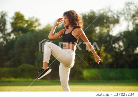 View from the side, doing fitness exercises. Young fitness woman is on the field outdoors View from the side, doing fitness exercises. Young fitness woman is on the field outdoors 137828234