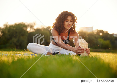 Sitting on the yoga mat. Young fitness woman is on the field outdoors Sitting on the yoga mat. Young fitness woman is on the field outdoors 137828236