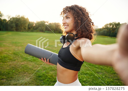 Holding camera and making selfie. Young fitness woman is on the field outdoors Holding camera and making selfie. Young fitness woman is on the field outdoors 137828275