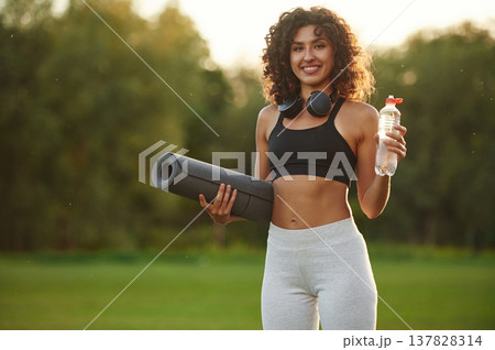 Hydration conception, holding bottle of water. Young fitness woman is on the field outdoors Hydration conception, holding bottle of water. Young fitness woman is on the field outdoors 137828314