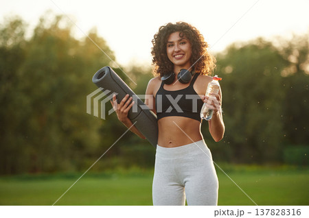Hydration conception, holding bottle of water. Young fitness woman is on the field outdoors Hydration conception, holding bottle of water. Young fitness woman is on the field outdoors 137828316