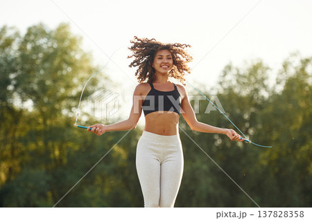 Jumping rope, active. Young fitness woman is on the field outdoors Jumping rope, active. Young fitness woman is on the field outdoors 137828358