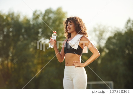 Drinking water from a bottle. Young fitness woman is on the field outdoors 137828362