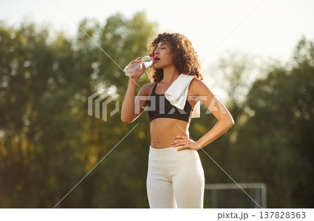Drinking water from a bottle. Young fitness woman is on the field outdoors 137828363