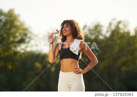 Drinking water from a bottle. Young fitness woman is on the field outdoors 137828365