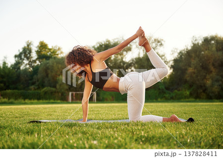 On the fitness mat, doing exercises. Young fitness woman is on the field outdoors On the fitness mat, doing exercises. Young fitness woman is on the field outdoors 137828411
