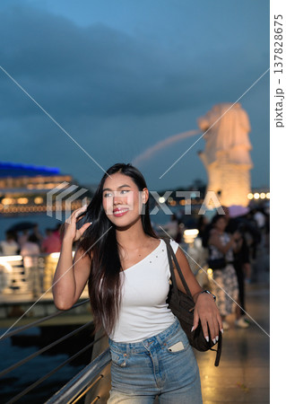 Asian tourist woman posing by the waterfront at Marina Bay Singapore during evening Asian tourist woman posing by the waterfront at Marina Bay Singapore during evening 137828675