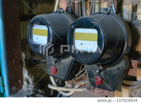 Two vintage, sealed electricity meters in an electrical panel in an old industrial building. The meters are connected to the power grid 137828938