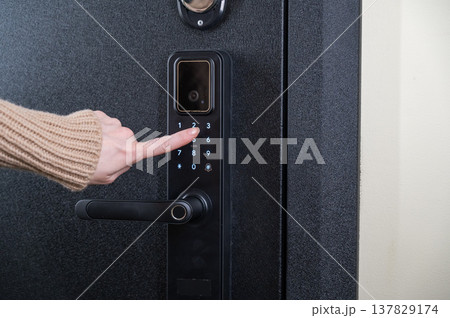 A woman opens a modern smart door lock with a digital keypad using a code. A woman opens a modern smart door lock with a digital keypad using a code. 137829174